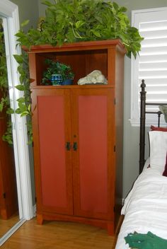 a wooden cabinet with plants on top of it in a bedroom next to a bed