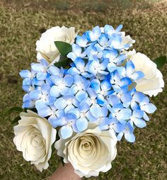 a bouquet of blue and white flowers in a vase on the ground with grass behind it