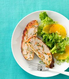 a white plate topped with meat and salad next to a fork on top of a blue table