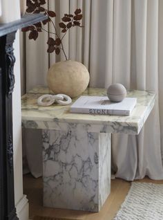 a marble table topped with a vase filled with flowers next to a book and other items