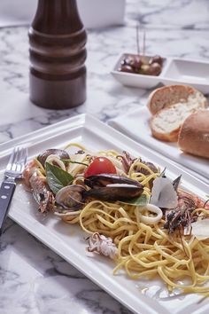 a white plate topped with pasta and clams on top of a table next to bread