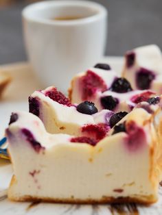 two slices of cheesecake with blueberries and whipped cream on top sitting on a plate next to a cup of coffee