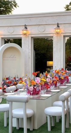 a long table with white chairs and flowers on it