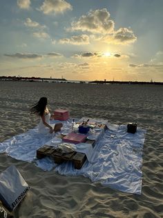 a woman sitting on top of a blanket on top of a sandy beach next to the ocean