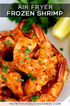 a white plate topped with cooked shrimp next to lemon wedges and cilantro