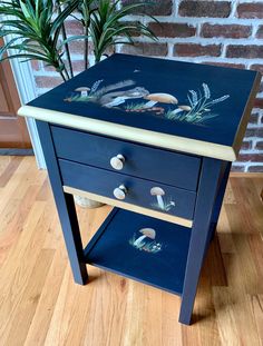 a blue side table with birds painted on it and two drawers underneath the drawer, next to a potted plant