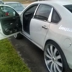 a white car with its door open in a parking lot next to other cars and grass