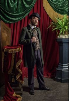 a man standing in front of a red curtain wearing a top hat and suit coat