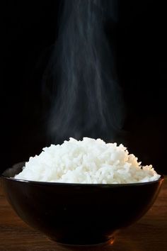 steaming rice in a black bowl on a wooden table