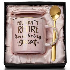 a pink coffee mug in a gift box with a gold spoon and fork next to it