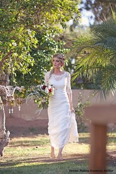 a woman in a white wedding dress walking through the grass with her bouquet on her hand