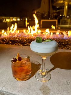 two cocktails sitting on top of a table next to a fire pit