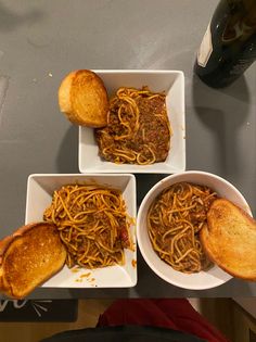 three white bowls filled with spaghetti and bread