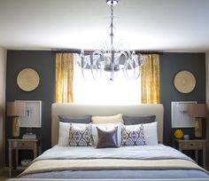 a large bed sitting under a window next to two nightstands and a chandelier