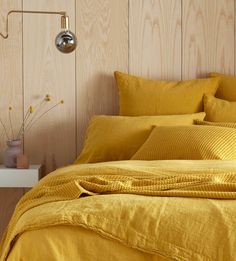 a bed with yellow linens and pillows in a small room next to a wooden wall