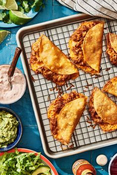 some tacos are sitting on a cooling rack next to bowls of guacamole and salsa