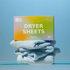 a box of dryer sheets sitting on top of a pile of folded towels in front of a blue background