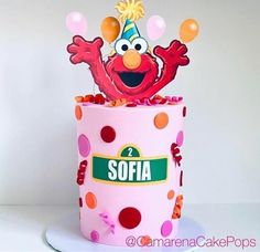 a pink birthday cake decorated with polka dots and an elm street sesame character on top