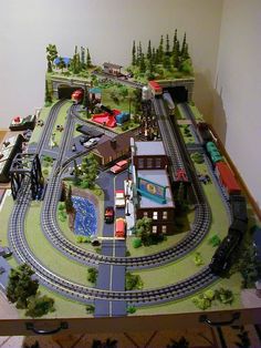 a model train set is displayed on a table with toy cars and trains around it