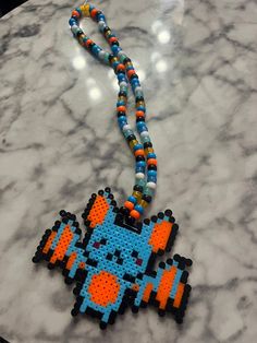 a necklace made out of perler beads on a marble counter with an orange and blue pacman bead