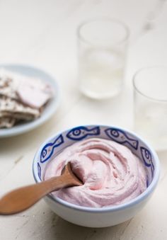 a bowl filled with pink ice cream next to two plates of crackers and glasses