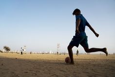 a young man kicking a soccer ball on top of a sandy beach next to the ocean