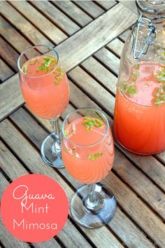 two glasses filled with pink liquid sitting on top of a wooden table next to a bottle