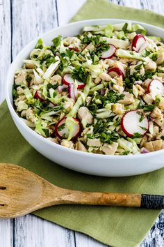 a salad with radishes and chicken in a white bowl next to a wooden spoon