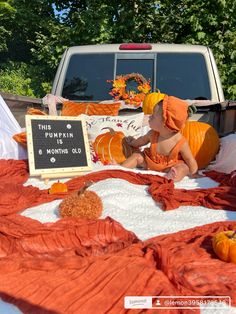 a baby sitting on the ground in front of a sign that says this pumpkin is for mommy's old