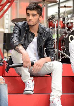 a man sitting on top of a red box next to a drum set and drums