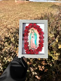 a person holding up a framed photo with roses in front of the virgin mary on it