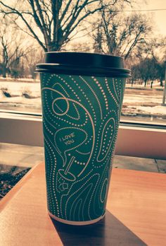 a coffee cup sitting on top of a wooden table next to a snow covered field