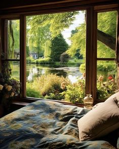 a bed sitting in front of a window next to a lush green forest filled with flowers