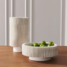 two white ceramic vases sitting on top of a wooden table next to each other