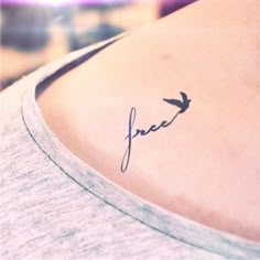 a small tattoo on the back of a woman's shoulder that reads free with a bird flying above it