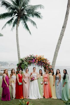 a group of women standing next to each other in front of palm trees and flowers