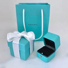 a blue gift bag with a white bow on the front and an open box in the back