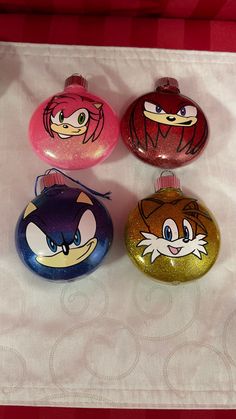 three glass ornaments with cartoon characters on them are sitting on a white sheet and red background