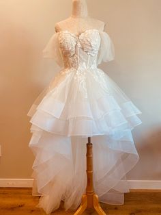 a white dress on a mannequin stand in front of a wall and wooden floor