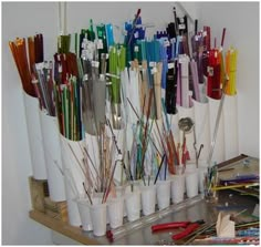 there are many pens and pencils in cups on the shelf next to each other