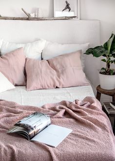 a bed with pink sheets and pillows on top of it next to a potted plant