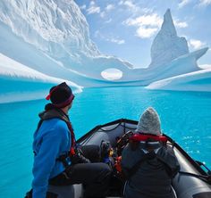 two people in a boat looking at an iceberg