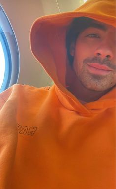 a man in an orange hoodie is looking at the camera while sitting on an airplane