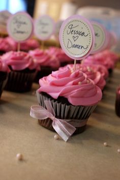 some cupcakes with pink frosting and small signs on top are sitting on a table