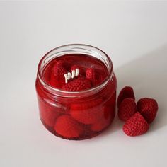 a jar filled with raspberries sitting on top of a white table next to another jar