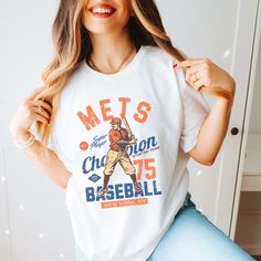 a woman wearing a mets t - shirt poses for a photo in front of a white wall