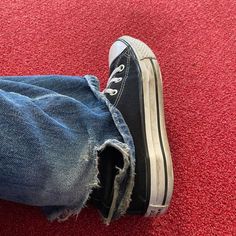 a person with ripped jeans and black sneakers is standing on a red carpeted area