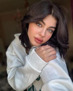 a woman in a white jacket posing for the camera with her hand on her shoulder