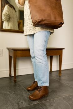 a woman standing in front of a mirror holding a brown bag