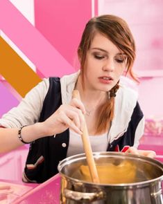 a woman stirring something in a pot with a wooden spoon on the counter next to her